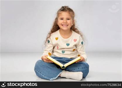 reading, education and childhood concept - beautiful smiling girl sitting on floor and reading book over grey background. beautiful smiling girl reading book on floor