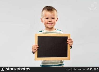 reading, education and childhood concept - portrait of smiling little boy holding black chalk board over grey background. portrait of smiling boy holding black chalk board