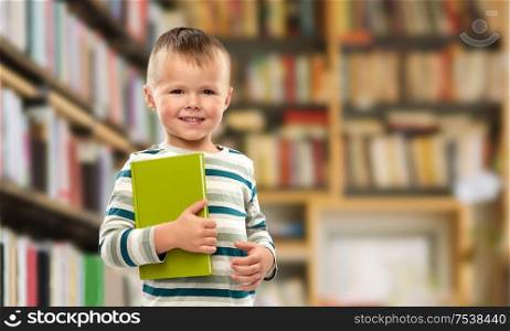reading, education and childhood concept - portrait of smiling little boy holding book over library background. portrait of smiling boy holding book over library