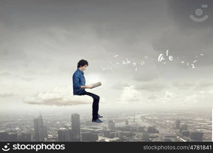 Reading favourite book in isolation. Young handsome man sitting on cloud and reading book