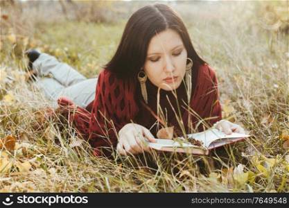 Reading girl is lying in fall grass