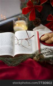 reading, holidays and leisure concept - close up of open book and glasses on christmas at home. close up of open book and glasses on christmas