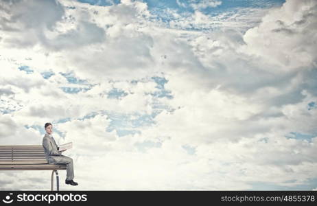 Reading in isolation. Young businessman sitting on bench with book in hands