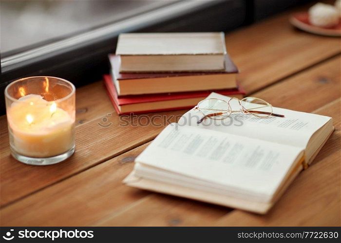 reading, leisure and objects concept - books, glasses and candle burning on window sill. books, glasses and candle burning on window sill