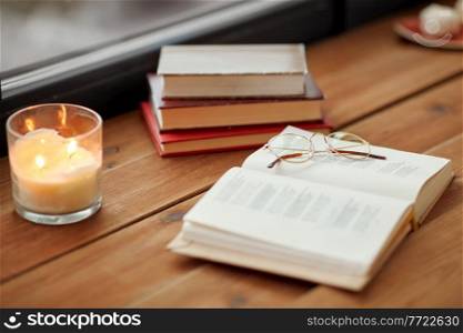 reading, leisure and objects concept - books, glasses and candle burning on window sill. books, glasses and candle burning on window sill