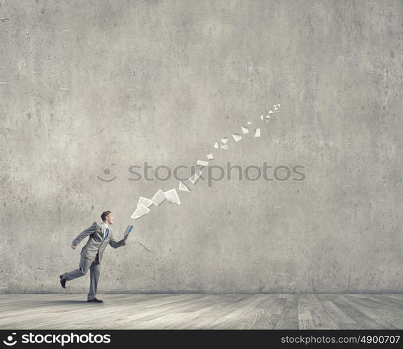 Reading on the run. Young businessman running with book in hand and pages flying in air