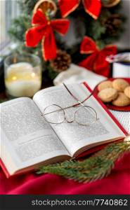 reading, winter holidays and leisure concept - close up of open book with glasses, fir branch, cookies and christmas decorations on window sill at home. close up of open book and glasses on christmas