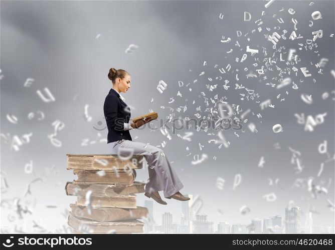 Reading woman. Young attractive woman sitting on pile of books and reading