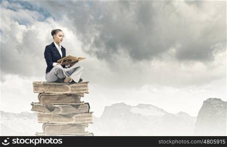 Reading woman. Young attractive woman sitting on pile of books and reading