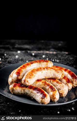 Ready grilled sausages on a plate. On a black background. High quality photo. Ready grilled sausages on a plate.