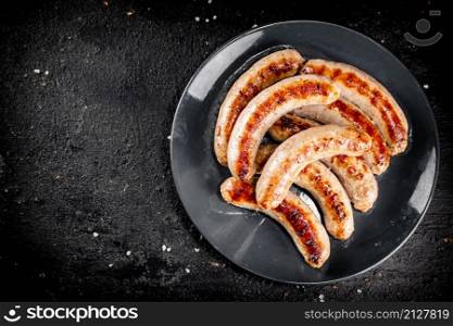 Ready grilled sausages on a plate. On a black background. High quality photo. Ready grilled sausages on a plate.