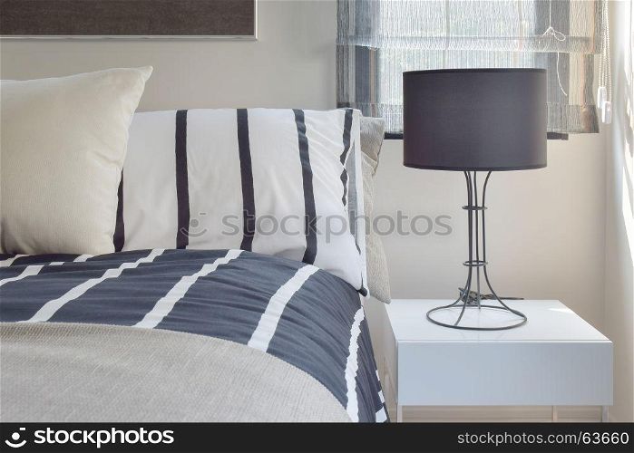 Ready lamp with black shade lamp on bedside table with striped pattern bedding