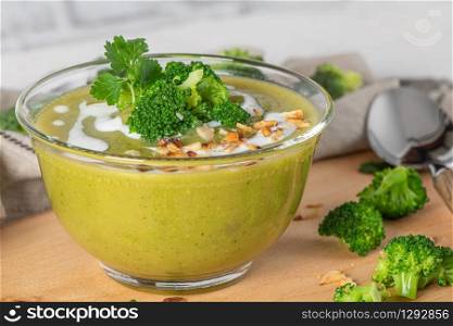 Ready to eat fresh hot broccoli puree soup with pieces of broccoli and basil leaves in a wooden plate on a wooden table. Close-up. Healthy eating and lifestyle.