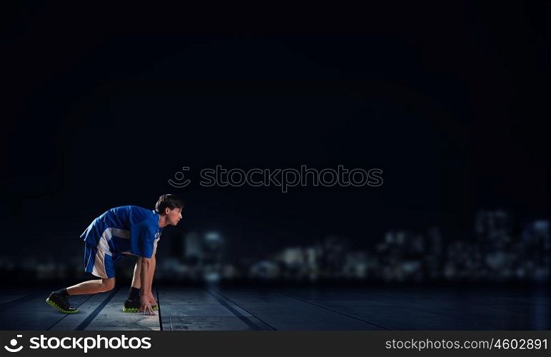 Ready to run. Athlete man in start pose on black background
