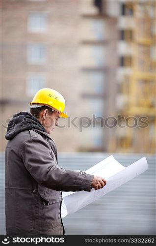 real builder with blueprints on construction site, natural light, focus on foreground