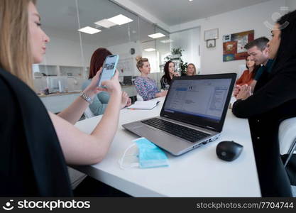 real businesswoman as a business leader checking smartphone email messages on team meeting in new normal coronavirus pandemic time protective medical face mask on desk