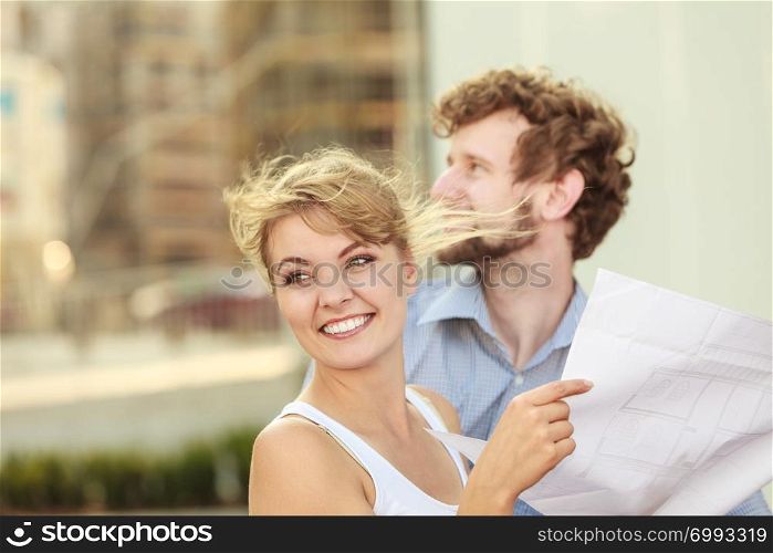 Real estate and family concept - young couple looking at blueprint project building plans dreaming about new house in modern residential area, construction site in the background. couple with blueprint project outdoor