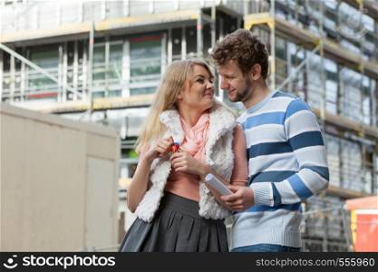 Real estate and family concept - young couple on front of new big modern house construction site with keys dreaming about home