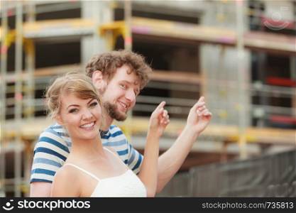 Real estate and family concept - young couple on front of new big modern house dreaming about home showing with fingers
