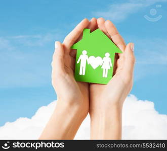 real estate and family home concept - closeup picture of female hands holding green paper house with family