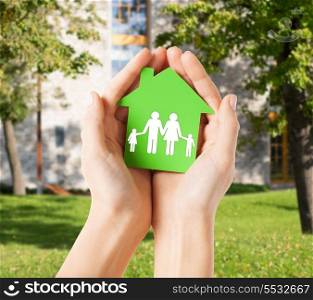 real estate and family home concept - closeup picture of female hands holding green paper house with family