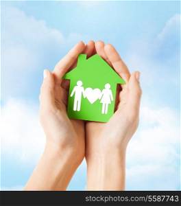 real estate and family home concept - closeup picture of female hands holding green paper house with family