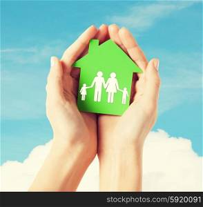 real estate and family home concept - closeup picture of female hands holding green paper house with family. hands holding green house with family