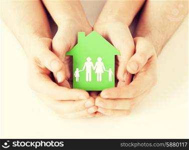 real estate and family home concept - closeup picture of male and female hands holding green paper house with family