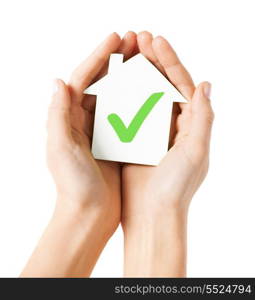 real estate and family home concept - hands holding paper house with green check mark