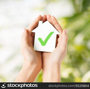 real estate and family home concept - hands holding paper house with green check mark