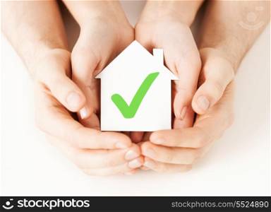 real estate and family home concept - male and female hands holding paper house with green check mark