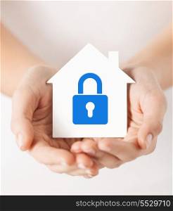 real estate and family home security concept - closeup picture of female hands holding white paper house with blue lock