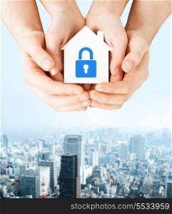 real estate and family home security concept - closeup picture of male and female hands holding white paper house with blue lock
