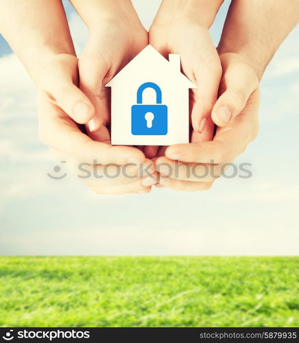 real estate and family home security concept - closeup picture of male and female hands holding white paper house with blue lock