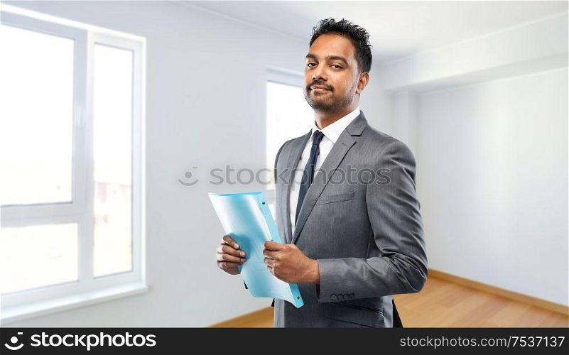 real estate business and people concept - indian man realtor with folder over empty new apartment room background. indian man realtor with folder at new apartment