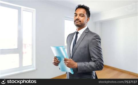 real estate business and people concept - indian man realtor with folder over empty new apartment room background. indian man realtor with folder at new apartment
