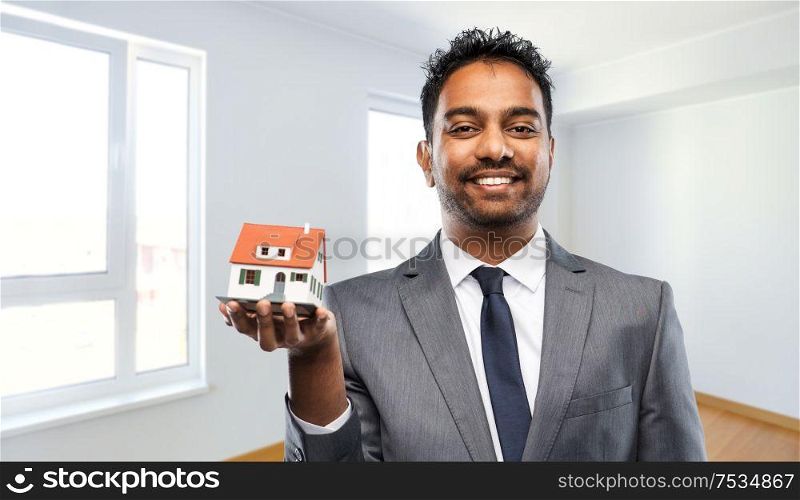 real estate business and people concept - indian man realtor with house model over empty new apartment room background. indian man realtor with house model at new home