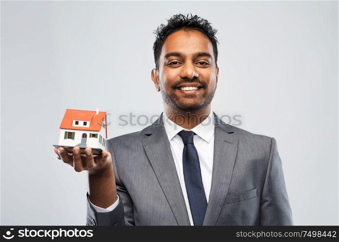 real estate business and people concept - indian man realtor with house model over grey background. indian man realtor with house model and folder