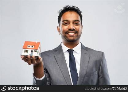 real estate business and people concept - indian man realtor with house model over grey background. indian man realtor with house model and folder