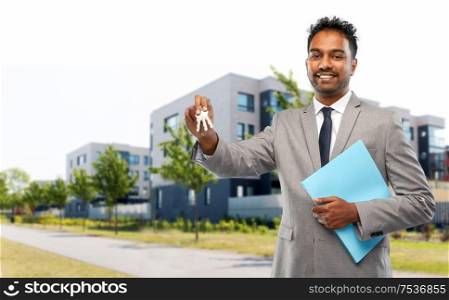 real estate business and people concept - indian man realtor with key and folder over living houses on city street background. indian man realtor with key and folder in city