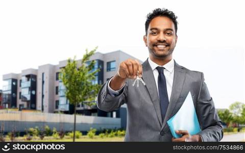 real estate business and people concept - indian man realtor with keys and folder over living houses on city street background. indian man realtor with home keys on city street