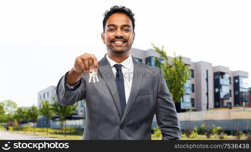 real estate business and people concept - indian man realtor with keys over living houses on city street background. indian man realtor with keys on city street
