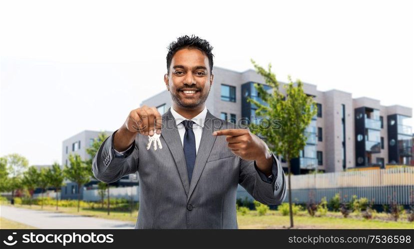 real estate business and people concept - indian man realtor with keys over living houses on city street background. indian man realtor with home keys on city street