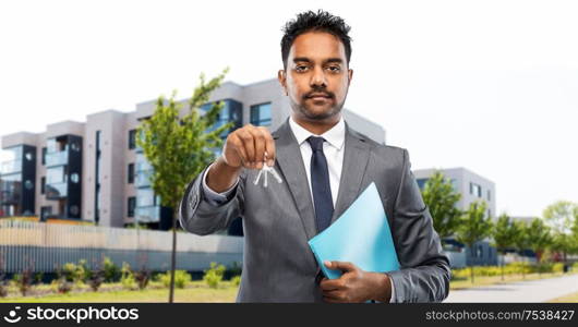 real estate business and people concept - indian man realtor with keys and folder over living houses on city street background. indian man realtor with home keys on city street