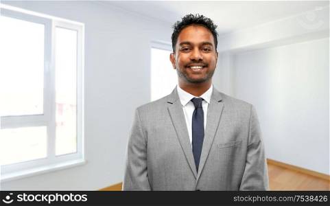 real estate business and people concept - smiling indian man realtor over empty new apartment room background. smiling indian man realtor at new apartment