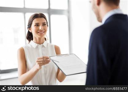 real estate business, sale and people concept - female realtor with clipboard showing contract document to customers at new office room. realtor showing contract document to customer. realtor showing contract document to customer