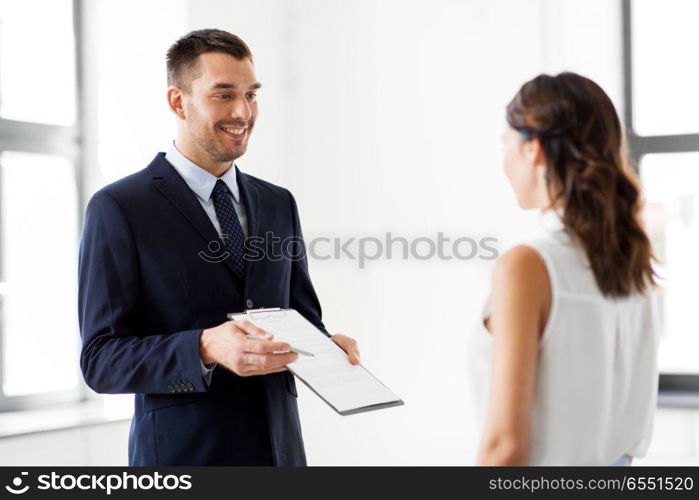 real estate business, sale and people concept - male realtor with clipboard showing contract document to customers at new office room. realtor showing contract document to customer. realtor showing contract document to customer