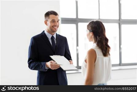 real estate business, sale and people concept - male realtor with clipboard showing contract document to customers at new office room. realtor showing contract document to customer. realtor showing contract document to customer