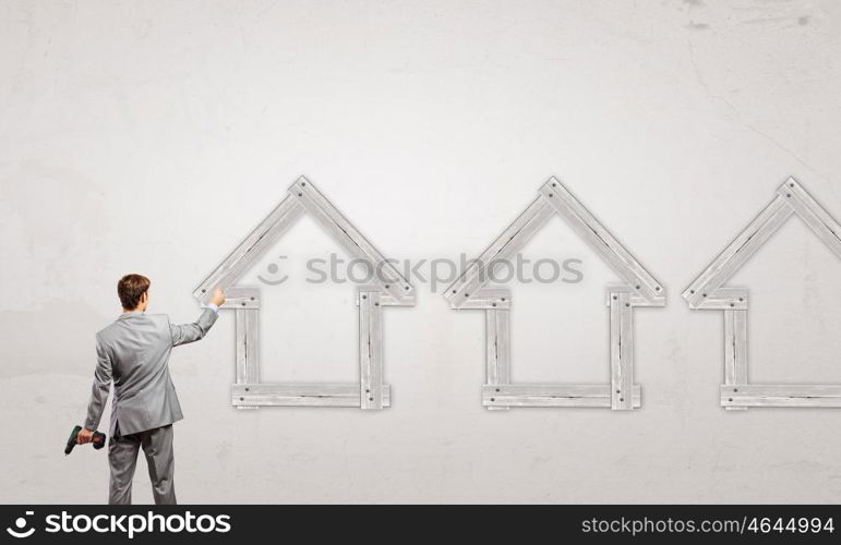 Real estate concept. Rear view of businessman fixing wooden house with drill