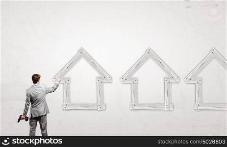 Real estate concept. Rear view of businessman fixing wooden house with drill